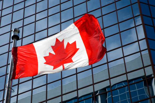 u 1 - Edwards Law An image showing a Canadian flag blowing in the wind in front of a corporate office building to show that permanent residency for skilled workers with gained valuable work experience in Canada can access such programs to get a faster path to permanent residency.